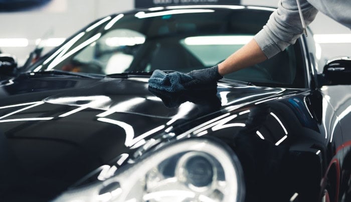 Man using a microfiber cloth to apply ceramic coating onto a shiny expensive black car. Unrecognizable person in protective gloves.